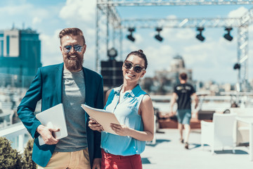 Poster - Portrait of cheerful bearded male and outgoing lady speaking while looking at camera. He holding laptop in hands and she keeping documents