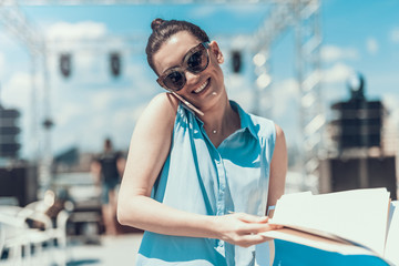 Poster - Portrait of beaming girl telling on contemporary mobile while flipping through documents. She walking outside during conversation with gadget