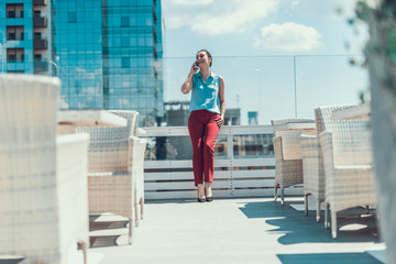 Poster - Full length portrait of outgoing female talking on mobile while relaxing outdoor. She putting hand in pocket of trousers