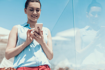 Poster - Low angle portrait of beaming female typing in phone while having rest outside