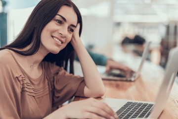 Poster - Portrait of outgoing girl typing on laptop at desk while touching head with arm. Cheerful lady during work concept