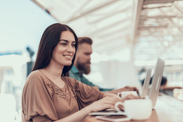 Poster - Portrait of pleased woman using notebook computer while locating at table in cafe. Male having job with gadget near her. Glad girl having labor with appliance during rest concept