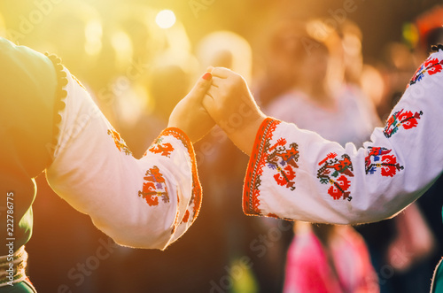 Fotomural Girls in traditional Bulgarian ethnic costumes with red dresses and patterns on white shirts holding hands in the sunset