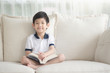 © lalalululala - Cute Asian boy reading a book on a sofa in living room