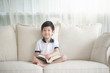 © lalalululala - Cute Asian boy reading a book on a sofa in living room