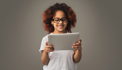 Cute black child girl using tablet ob studio background