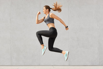 active woman being full of energy, jumps high in air, wears sportsclothes, prepares for sport compet