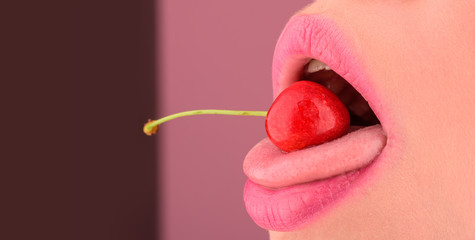 Erotic tongue. Red cherry lies on mouth of young female. Sensual photo with fruit. Seductive close up of woman open mouth with cherry inside. Red cherries between lips of young girl. Taste and diet