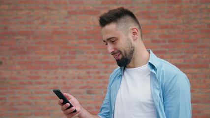 A man with a beard smiling against a brick wall background. Medium shot. Soft focus