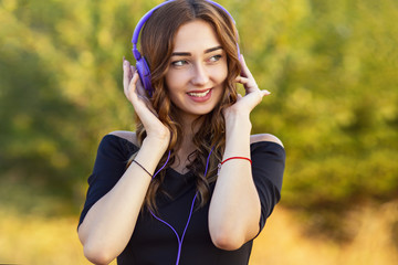 Wall Mural - portrait of a beautiful girl with headphones on head, young woman listening to music on the nature in the field