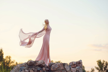 elegant princess with blond fair wavy hair with tiara on it, wearing a long light pink rose fluttering dress, standing on the tower of the castle at the sunset. feel free. pastel art. fly like a bird