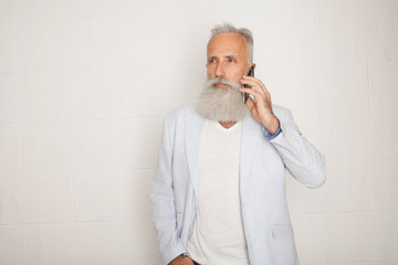 Wall Mural - Studio shot of happy senior bearded businessman smiling while using mobile phone with against white background