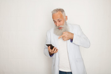 Wall Mural - Studio shot of happy senior bearded businessman smiling while using mobile phone with against white background