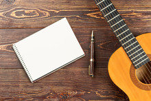 Guitar With Blank Notebook And Pen. Workspace With Blank Notebook, Pen And Acoustic Guitar On Brown Wooden Table Background. Work Space Of Songwriter.