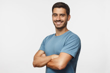 Portrait Of Attractive Young Sporty Man In Blue T-shirt Standing With Crossed Arms Isolated On Gray Background