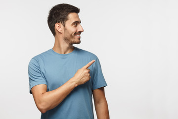 Wall Mural - casual dressed young man in blue t-shirt looking right, pointing with his finger, isolated on gray b