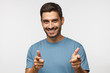 © Damir Khabirov - Young man isolated on gray background wearing blue t-shirt, smiling happily with open mouth and pointing to camera with both hands