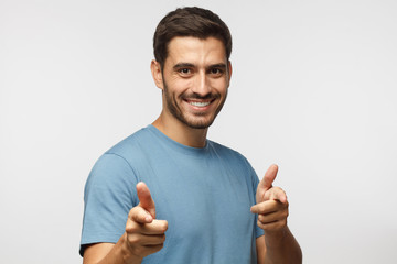 Wall Mural - hey you! young man in blue t-shirt pointing to camera with fingers isolated on gray background