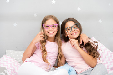 Birthday girl. Children posing with grimaces photo booth props. Pajamas party in bedroom. Friends cute and cheerful posing with eyeglasses accessories. Girls friends having fun pajamas party