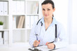 © rogerphoto - Young brunette female doctor at working place in  hospital. Health care, insurance and help concept