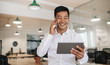 © mavoimages - Smiling Asian businessman using a cellphone and tablet at work