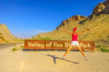 Young tourist girl jumping at welcome sign entrance of Valley of Fire State Park. Summer travel holidays in Nevada, United States. Valley of Fire is located in the Mojave Desert 58 miles of Las Vegas.