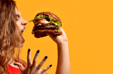 Woman hold big beef burger sandwich with hungry mouth happy screaming laughing on yellow background