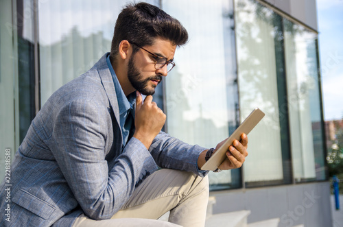 Fotografia Handsome macho man sitting on stairs in front of modern office building and look