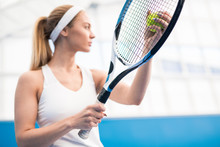 Low Angle Portrait Of Female Tennis Player Serving Ball And Holding Racket While Playing In Indoor Court