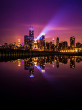 Beautiful Long Exposure Chicago Night Skyline Photo With Building Lights At Sunset With Pink Purple And Blue Clouds In The Sky Reflecting In A Calm Pool Of Water And Spotlight Shining Up Into The Sky.