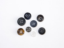 Close Up View Of Several Four Hole Sewing Or Clothing Buttons Of Random Shape Color And Size Isolated On A White Background.