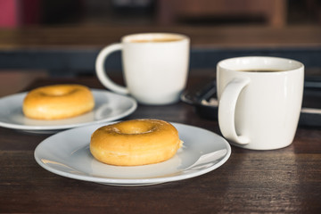 Two set of donuts in a white plate with coffee cups on wooden table