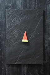 Wall Mural - A piece of fresh watermelon on a black slate on a dark concrete background with copy space. Vitamin dessert. Top view