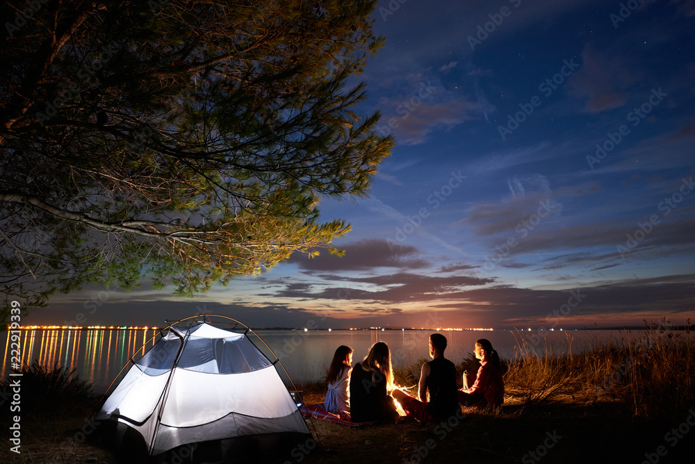 Back view of tourists, girls and boy having a rest on lake shore around ...