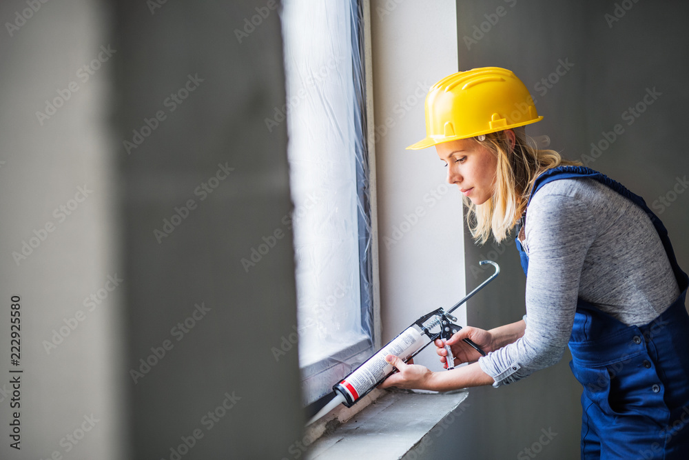 Young woman worker using silicone sealant gun on the construction site. - obrazy, fototapety, plakaty 