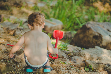 Child playing outdoors. Kid we pour the sand into the red truck. Children street games A boy playing with a machine on the big log