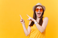Portrait Of Smiling Young Woman In Straw Summer Hat, Orange Glasses Pointing Index Fingers Aside Copy Space Isolated On Yellow Background. People Sincere Emotions, Lifestyle Concept. Advertising Area.