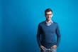 © Halfpoint - Portrait of a young man with glasses in a studio on a blue background.