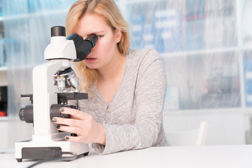 Wall Mural - Young woman medical researcher looking through microscop on slide