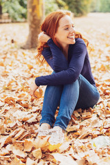 Poster - Happy woman sitting on autumn leaves in park