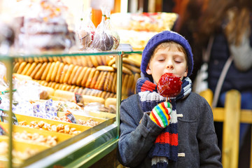 Wall Mural - Happy child eating on apple covered with red sugar on Christmas market