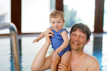 Wall Mural - Happy middle-aged father swimming with cute adorable baby girl in swimming pool.