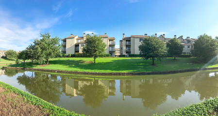 Wall Mural - Panorama view mirror reflection of typical riverside apartment building complex in Irving, Texas, USA. Urban eco living place with a lot of mature trees and canal