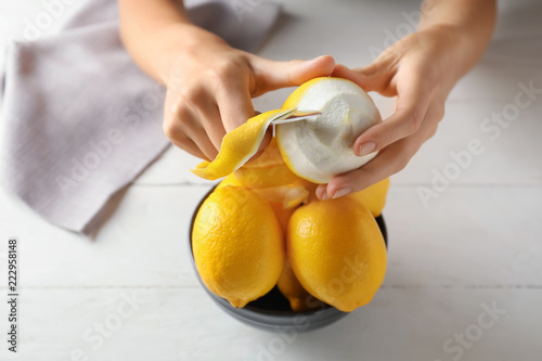 Cuadros en Lienzo Woman peeling ripe lemons at white wooden table, closeup