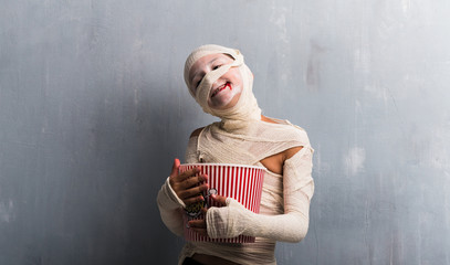 Wall Mural - Boy in mummy costume eating popcorns for halloween holidays