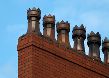 A Row Of Old Fashioned Traditional Clay Chimney Pots On A Red Brick Support Against A Blue Sky From When Houses Where Built Coal Burning Heating