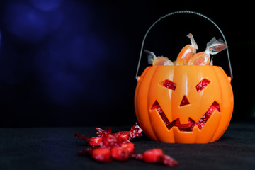 halloween Jack o Lantern candy collector full of candy and some scattered sweets on the black background