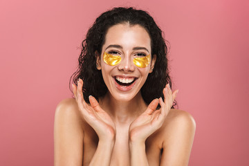 Sticker - Beauty portrait of european shirtless woman with long brunette hair wearing cosmetic patches under her eyes, isolated over pink background