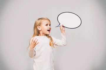 Little beautiful cute baby girl with a white cloud of thoughts in the form of a sign in the Studio on a gray background