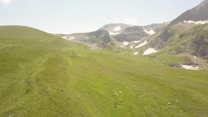 Wall Mural - people walking on summer meadow in valley and mountain landscape from drone